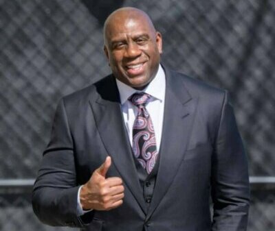Magic Johnson in a suit and tie giving a thumbs up.