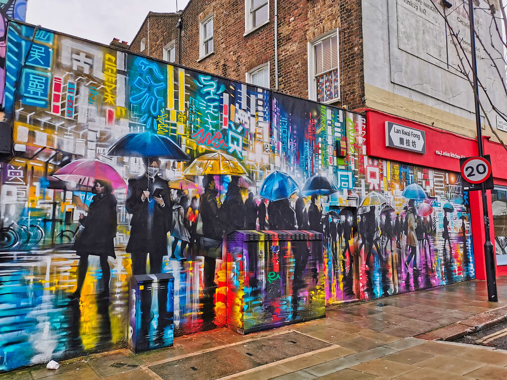 A colorful mural on a building with people holding umbrellas.