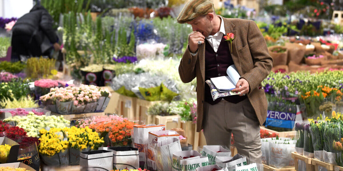 A man in a hat admiring flowers at a flower market.