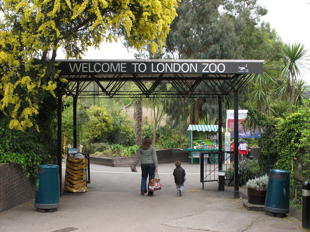 A woman and a child walking through the entrance to the london zoo.