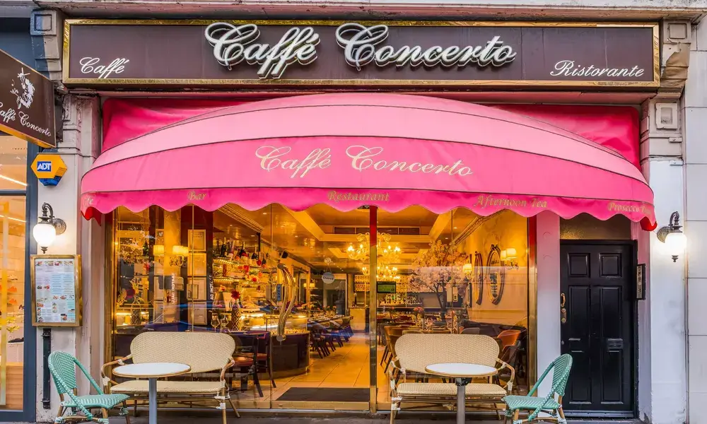 A cafe with a pink awning in front of it.