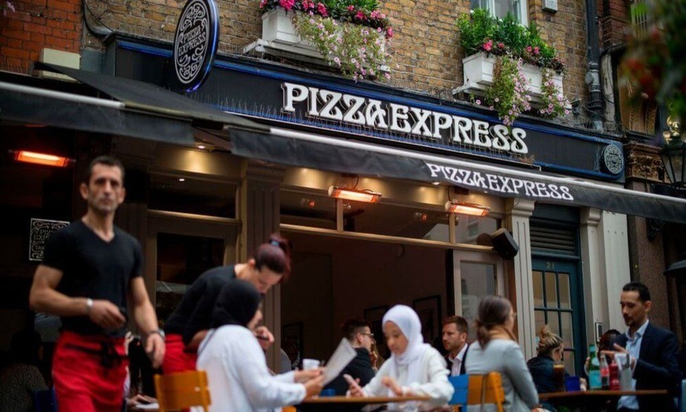 A group of people sitting outside a pizza express restaurant.