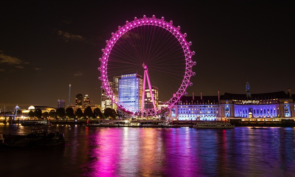 The london eye is lit up pink at night.