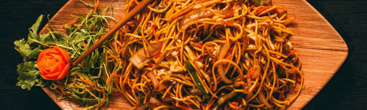 A plate of noodles and vegetables on a wooden board.