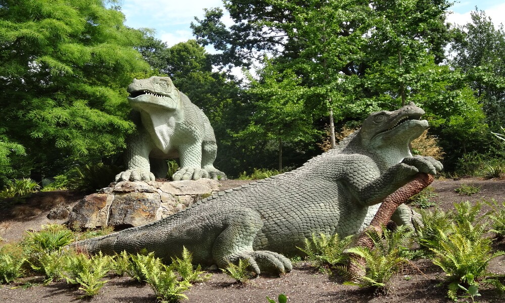 Two statues of dinosaurs in a park.