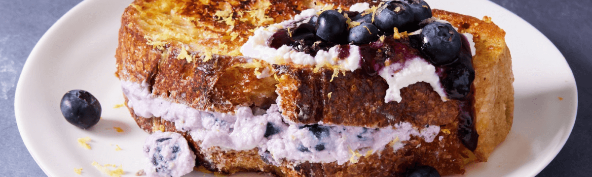 A plate of french toast with blueberries and whipped cream.
