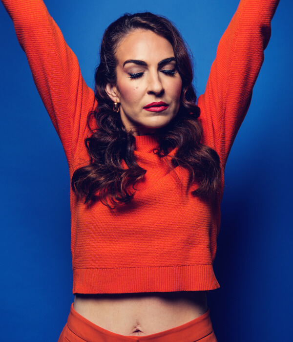 A woman in an orange sweater with her arms outstretched.