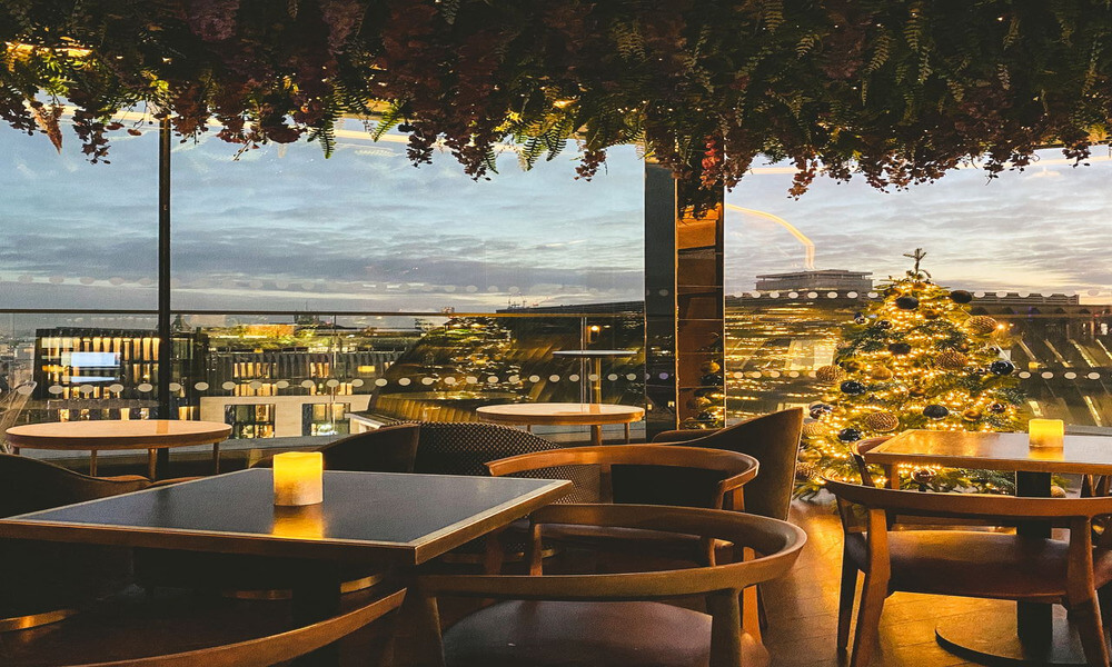 A restaurant with tables and chairs overlooking a city at dusk.