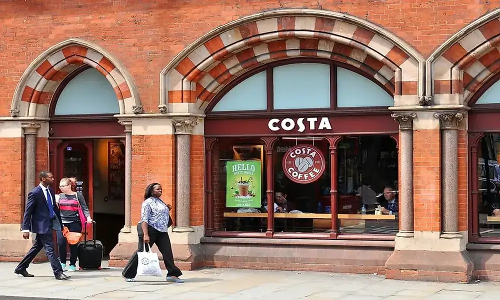 A group of people walking past a costa coffee shop.