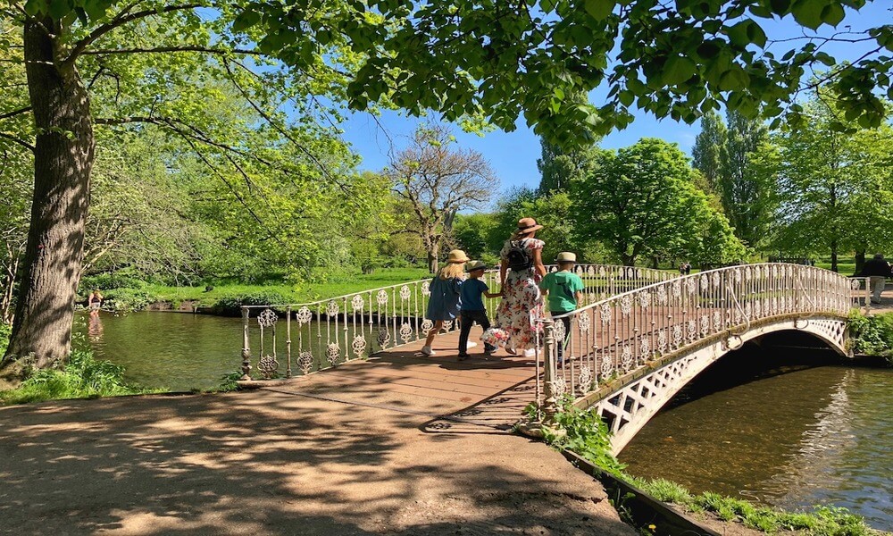 A group of people walking across a bridge in a park.