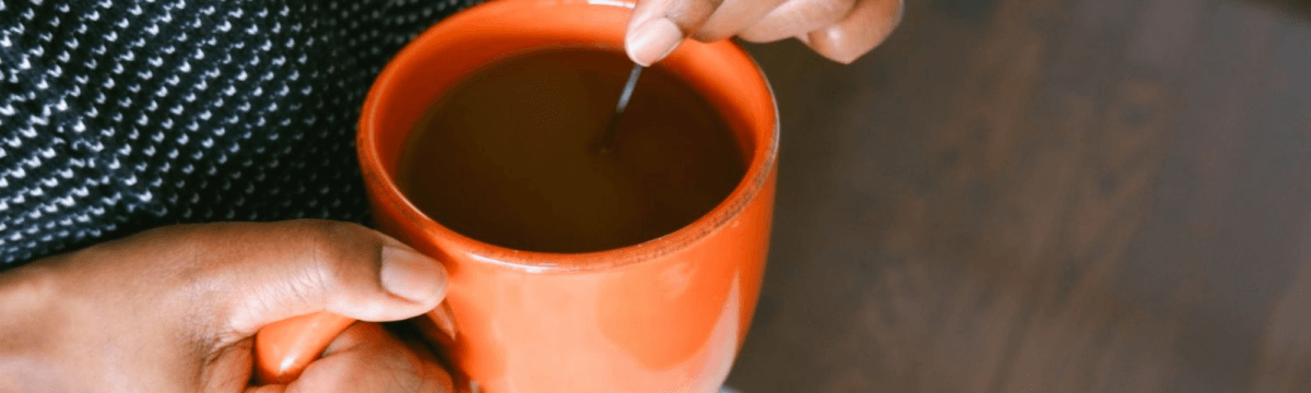 A person holding a cup of coffee with a spoon.
