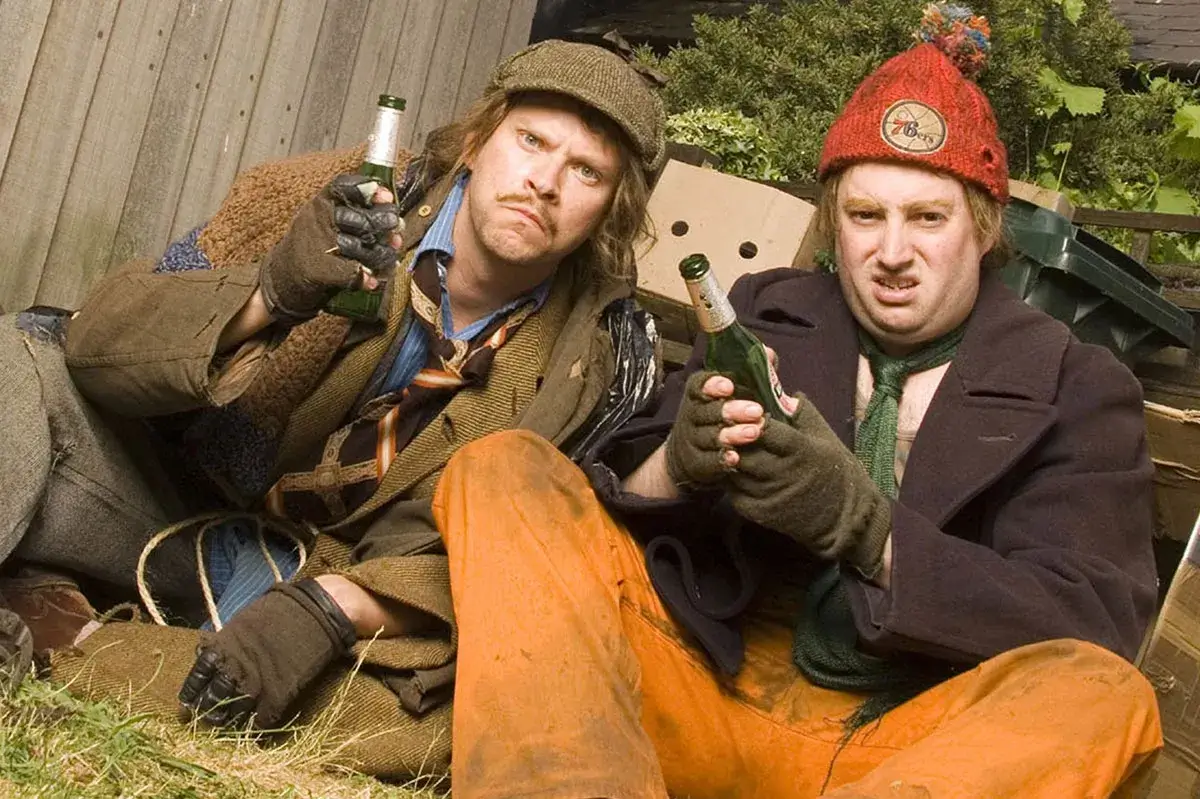 Two men sitting on the ground holding beer bottles.