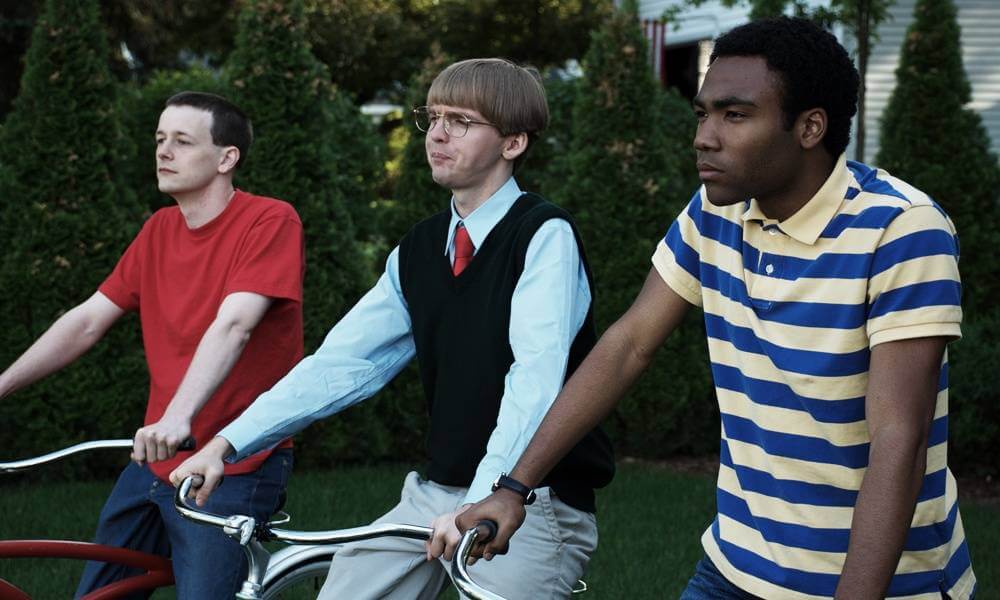 Three young men riding bicycles in a yard.