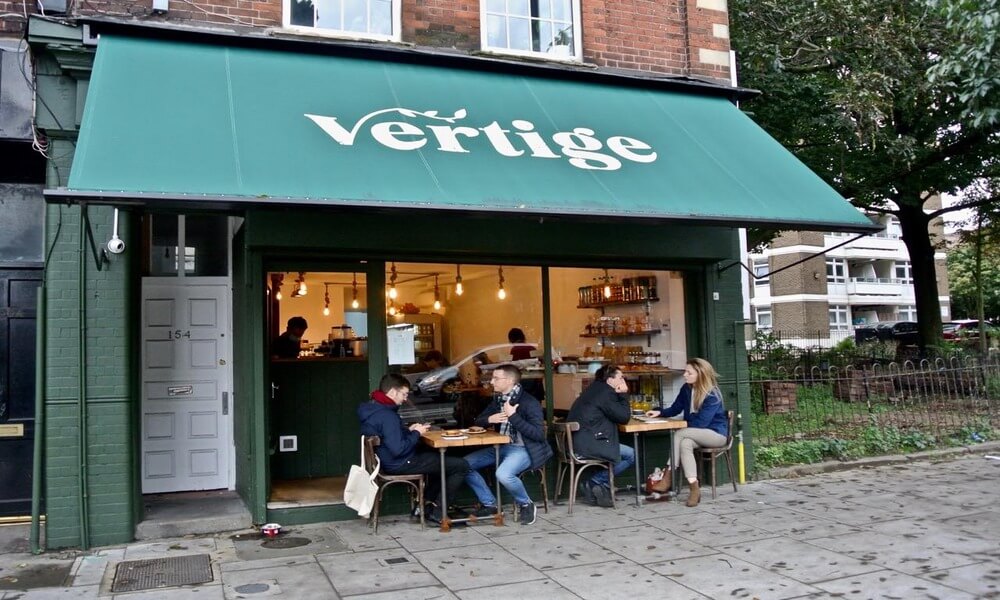 A group of people sitting outside of a vertigo cafe.