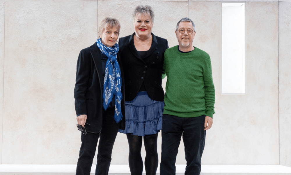 Three people posing for a picture in front of a white wall.