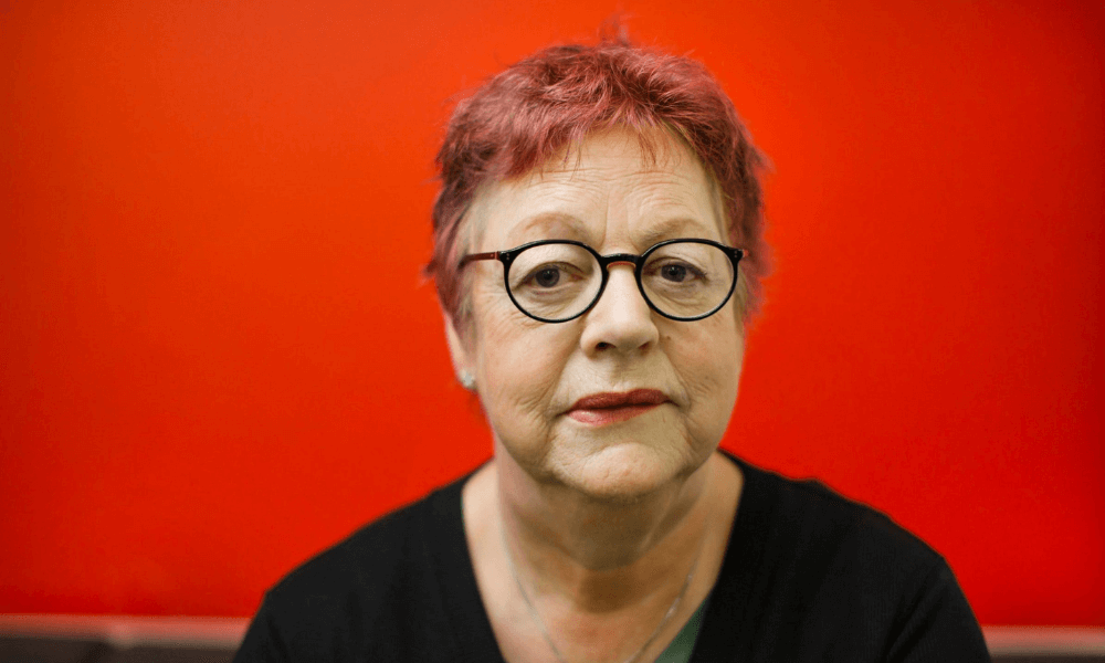 A woman wearing glasses in front of a red wall.