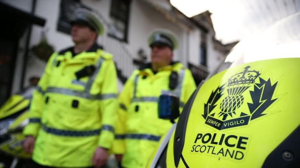 Police officers in high-visibility jackets with "police scotland" badge prominently displayed.