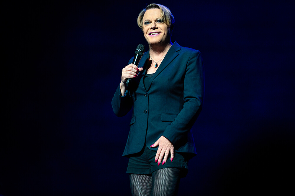 Performer in a black suit holding a microphone on stage.