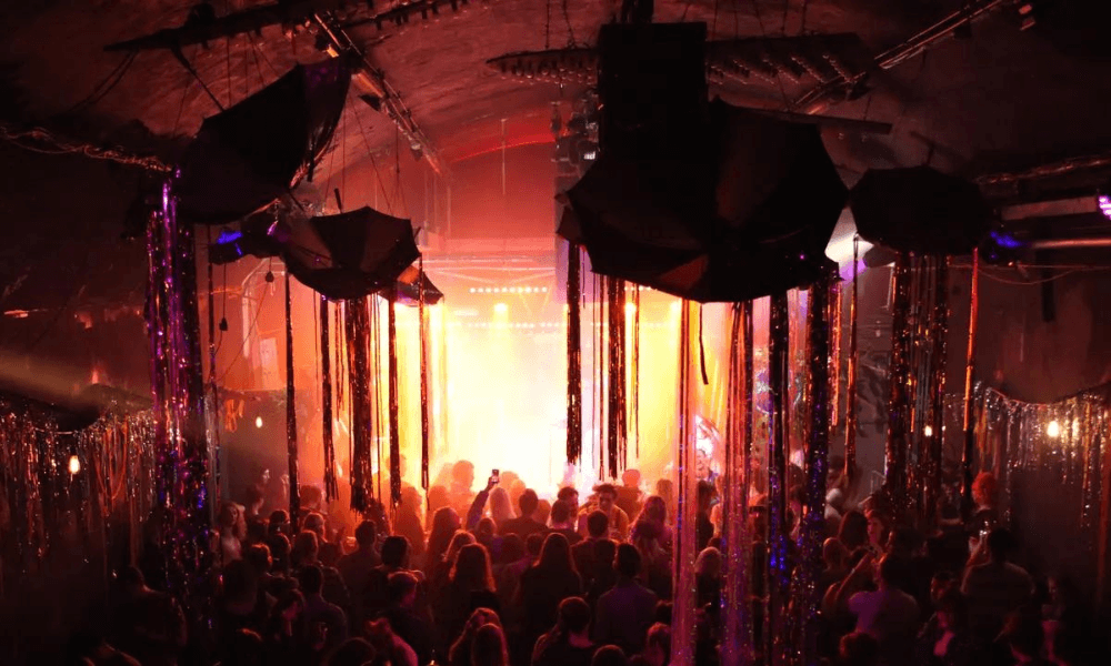 A vibrant nightclub atmosphere with a crowd enjoying the illuminated stage and festive decorations.