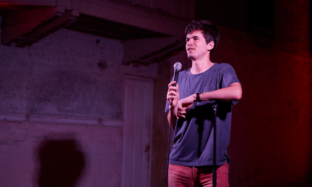 A young man performing stand-up comedy on stage with a microphone.