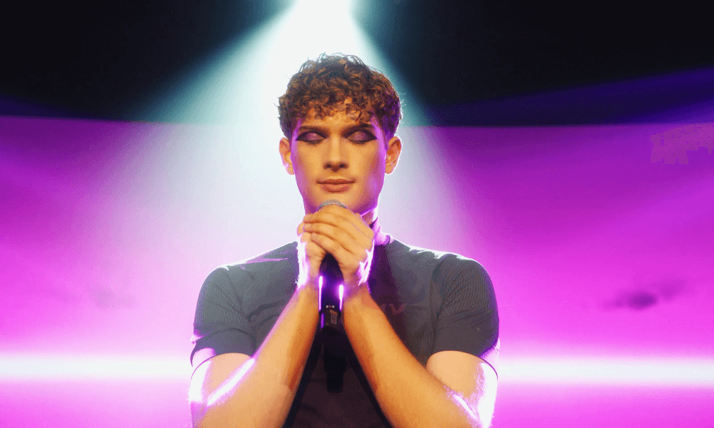 A young male singer on stage under a spotlight with a purple background.
