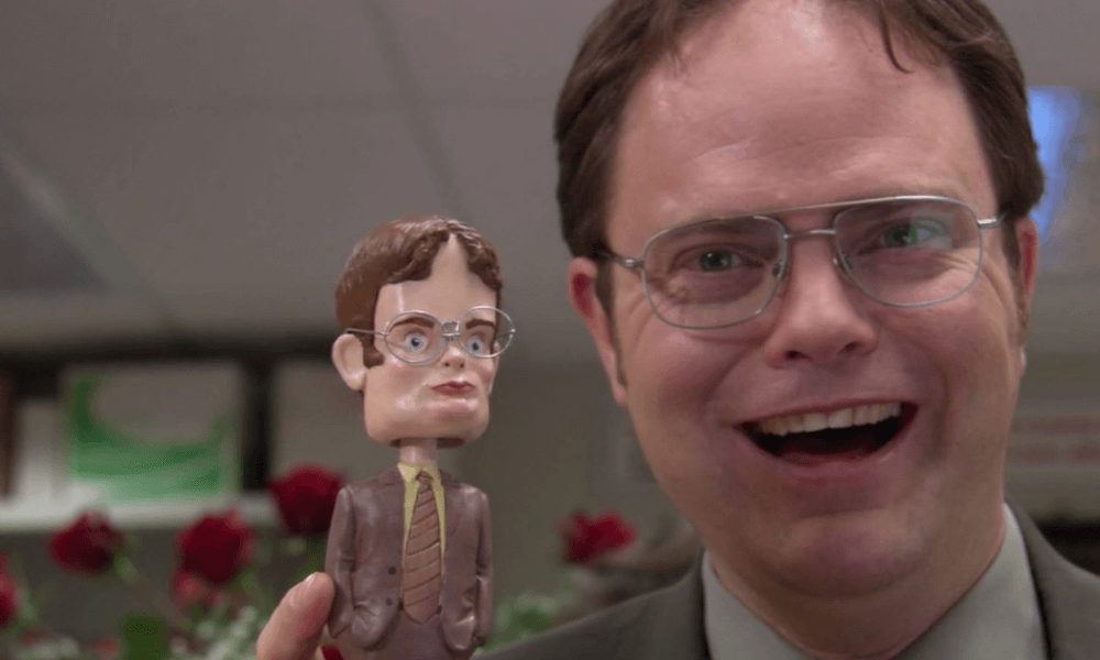 A man smiling while holding a bobblehead figurine that resembles him.