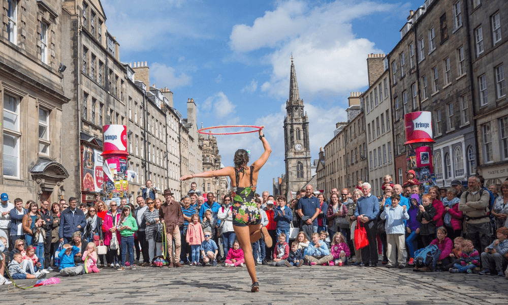A street performer hula hooping before an audience on a sunny day in an urban environment.