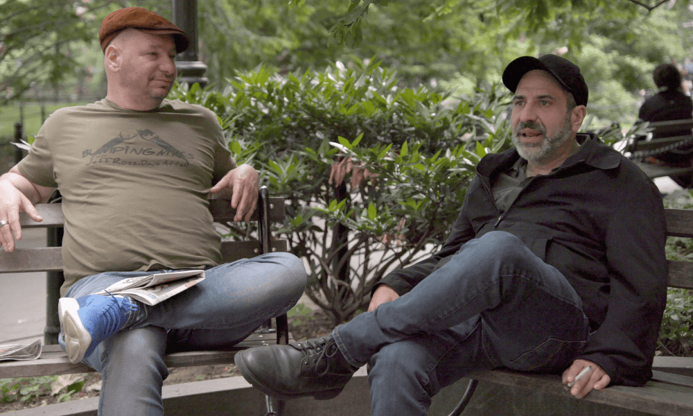 Two men sitting on a park bench engaged in conversation.