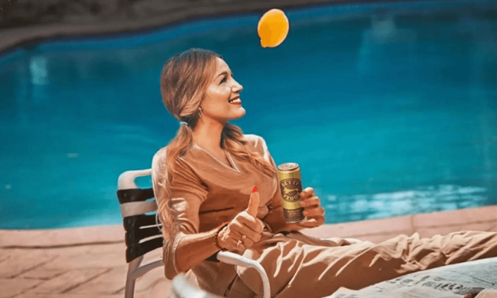 Woman smiling while tossing a lemon in the air by a swimming pool.