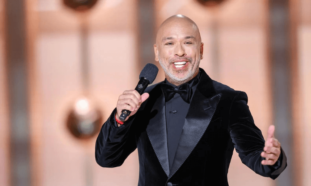 A bald man in a tuxedo is holding a microphone.