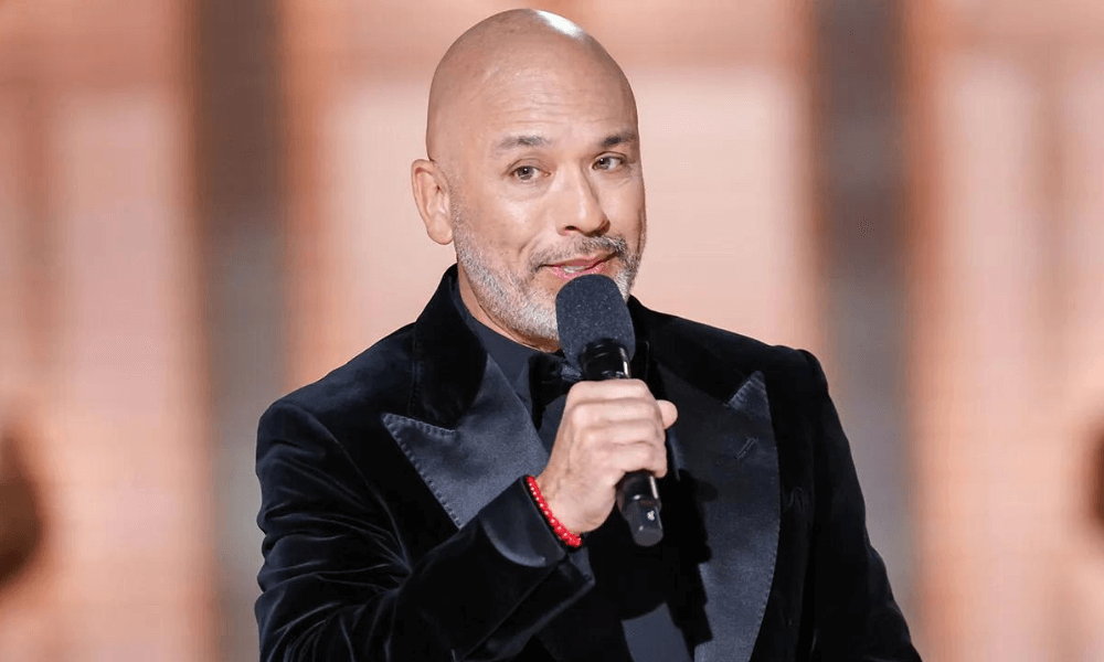 A bald man in a black suit is holding a microphone.