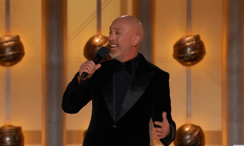 A bald man in a tuxedo singing into a microphone.