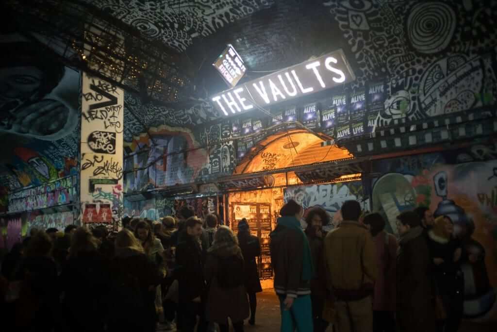Crowd gathers in front of "the vaults" venue with graffiti-covered walls at night.