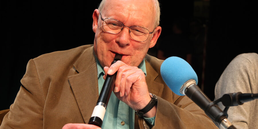 A man playing a recorder into a microphone on stage.