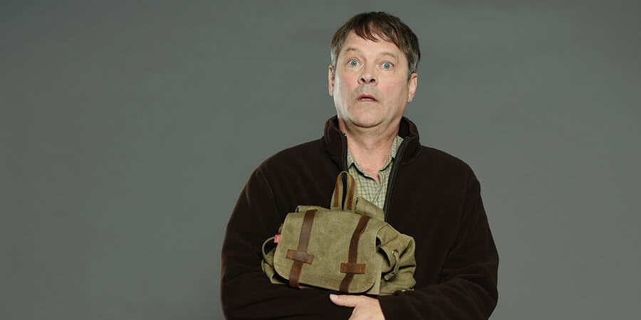 Man holding a satchel with a surprised expression against a gray background.
