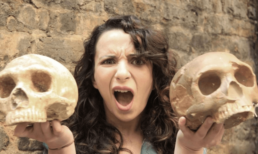 Woman holding two skulls with a surprised expression.