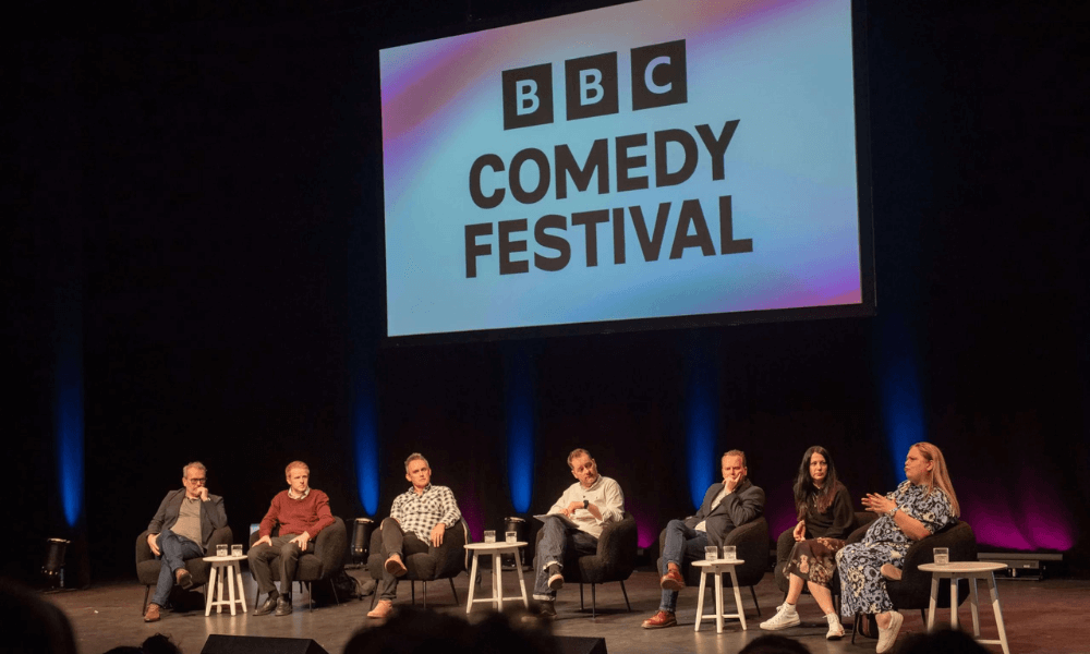 Panelists seated on stage during a bbc comedy festival event.