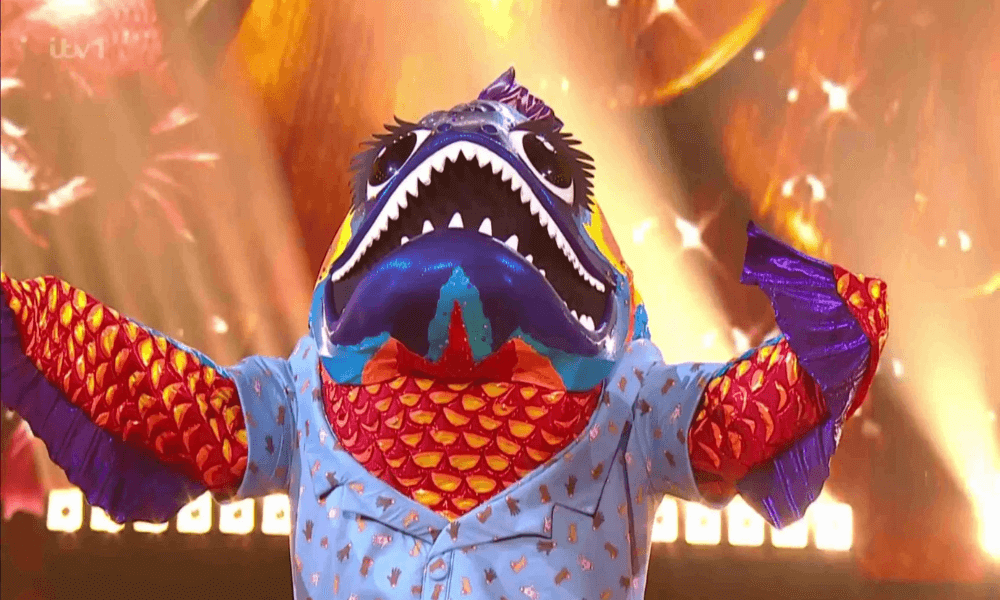 Person in a colorful shark costume performing on stage.