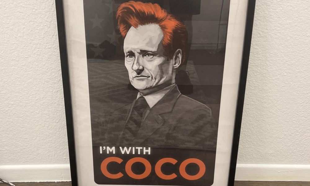Framed poster depicting a stylized illustration of conan o'brien with orange hair and the slogan "i'm with coco" on an orange banner, set against a background of stars.