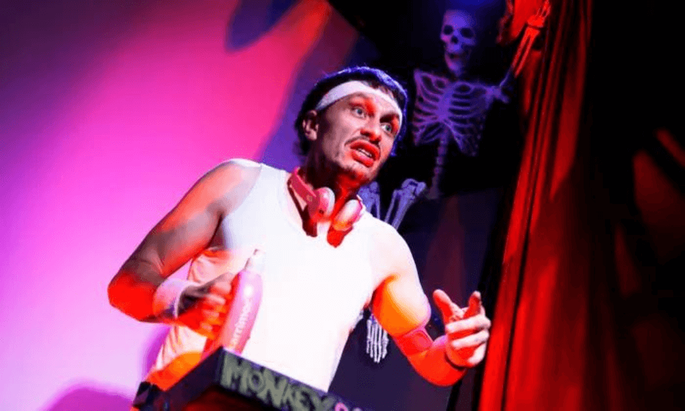 A performer dressed as a pirate, complete with a bandana and fake mustache, acts on stage beside a skeleton prop under red lighting.