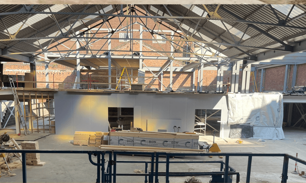Interior of a construction site with exposed steel beams and unfinished walls, featuring construction materials and tools scattered around.