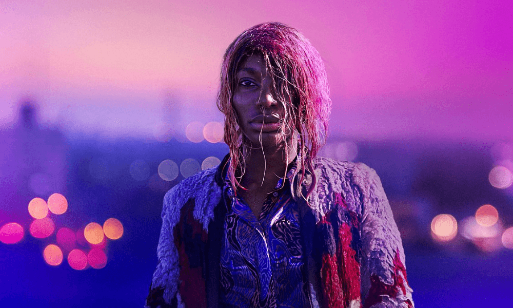 A young woman with wet hair stands against a cityscape at twilight, illuminated by purple and pink lights.