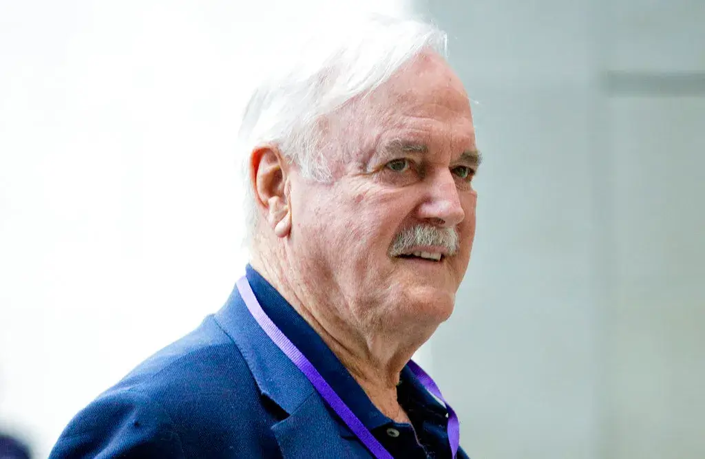 Senior man with white hair and mustache, wearing a navy blazer, walking in a hallway.