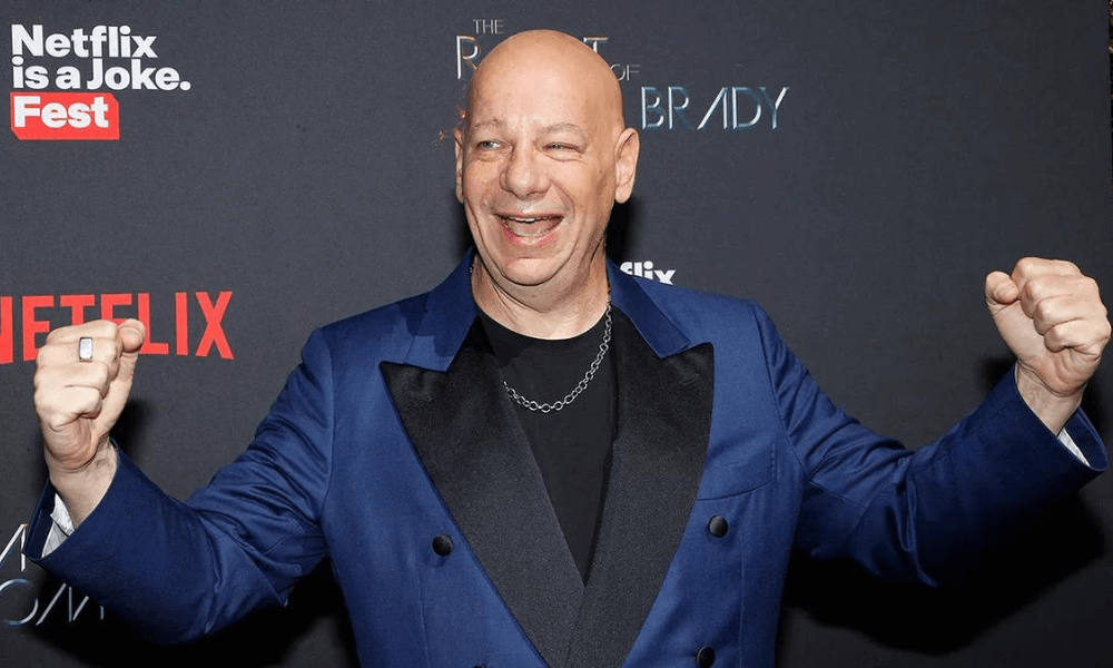 Man in a blue blazer and black shirt, smiling and raising fists in excitement at a netflix event.