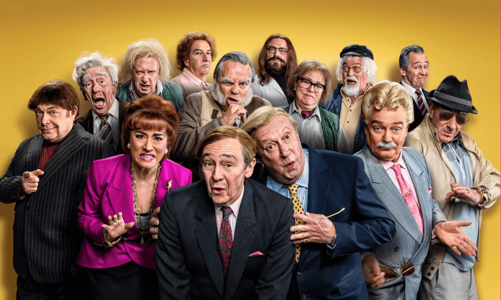 Group of diverse comedic actors in various costumes and expressions against a yellow background.